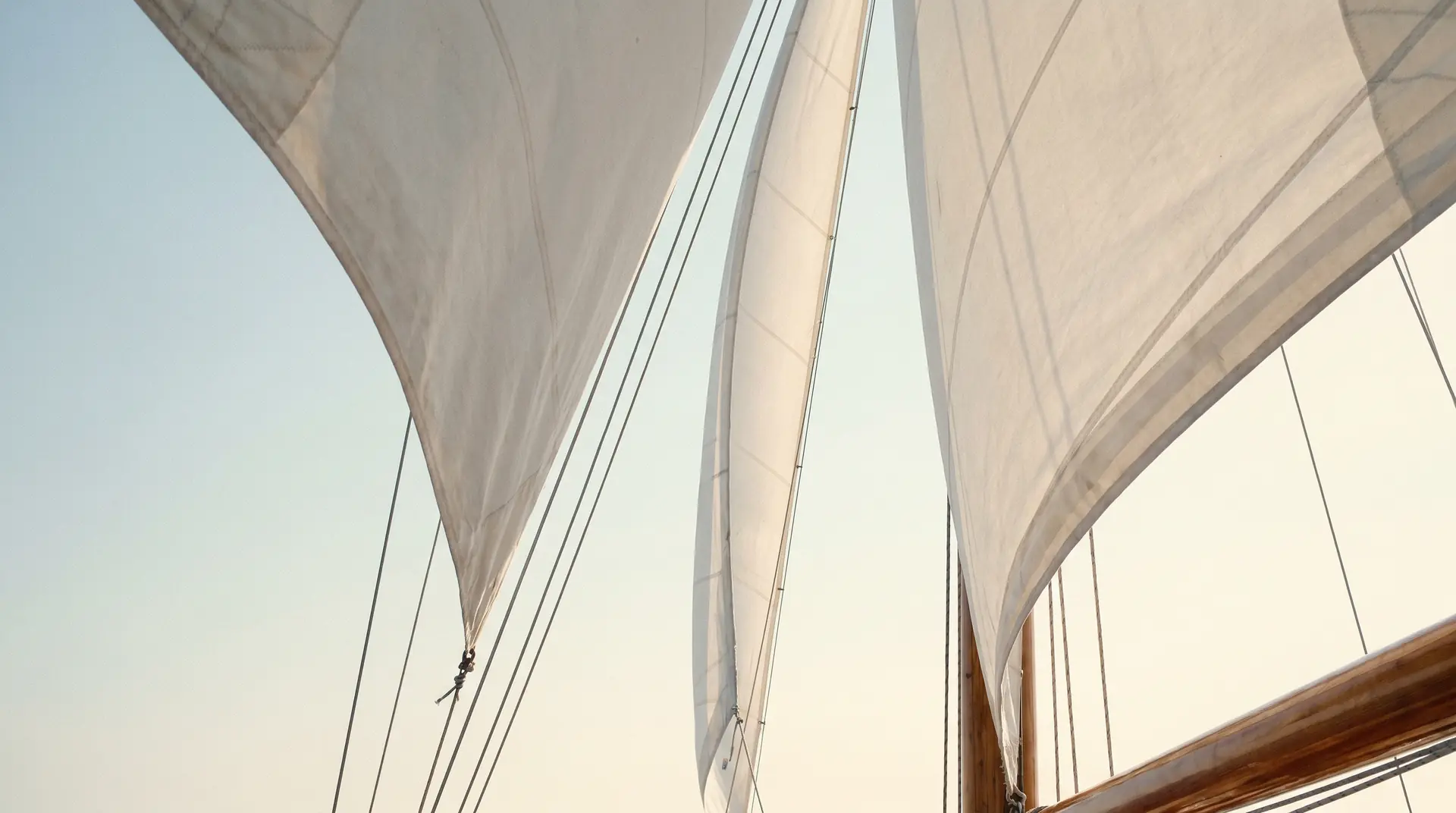 White sails drawn taut against a pale Aegean sky, seen from below